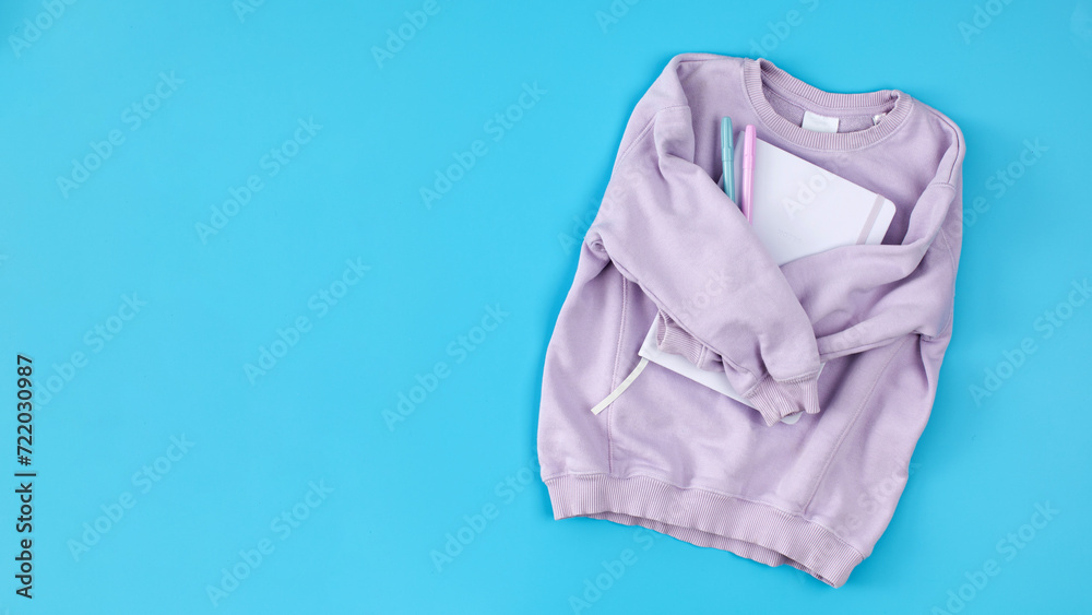 Lilac children's sweatshirt with a notebook on a blue. Copy space Lilac children's sweatshirt with a notebook on a blue. Copy space