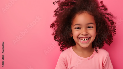A cheerful young girl with curly hair exudes happiness while standing against a vibrant pink background. © stocker