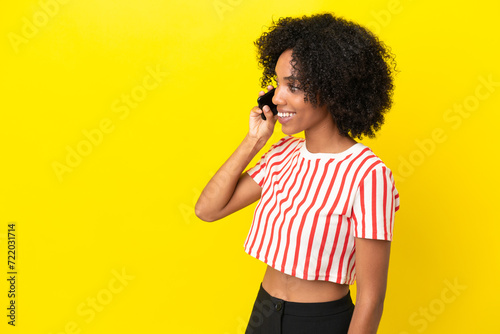 Young African American woman isolated on yellow background keeping a conversation with the mobile phone with someone