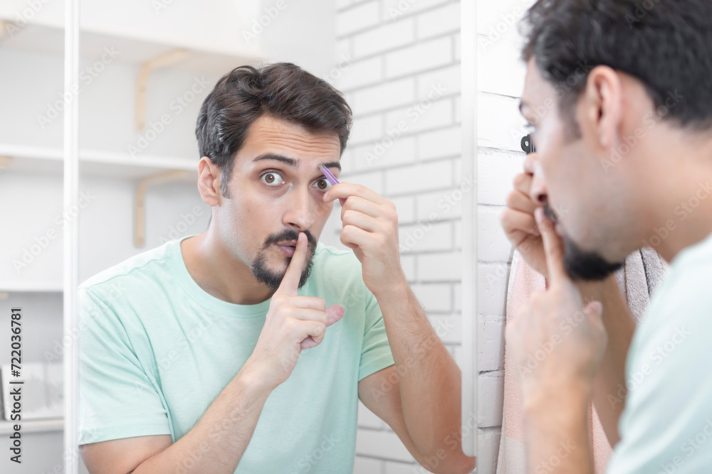 Handsome man grooming in front of the mirror in the bathroom. Young guy depilates with tweezers Handsome man grooming in front of the mirror in the bathroom. Young guy depilates with tweezers