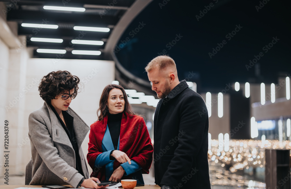 Three business colleagues engaging in a serious conversation over documents in a contemporary office space with city lights in the background. Three business colleagues engaging in a serious conversation over documents in a contemporary office space with city lights in the background.