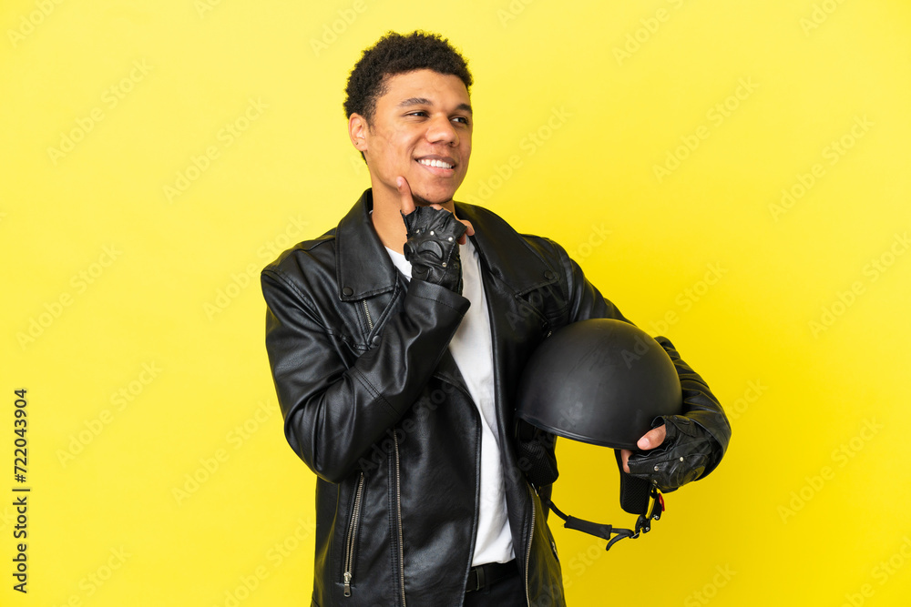 Young African American man with a motorcycle helmet isolated on yellow background thinking an idea while looking up Young African American man with a motorcycle helmet isolated on yellow background thinking an idea while looking up