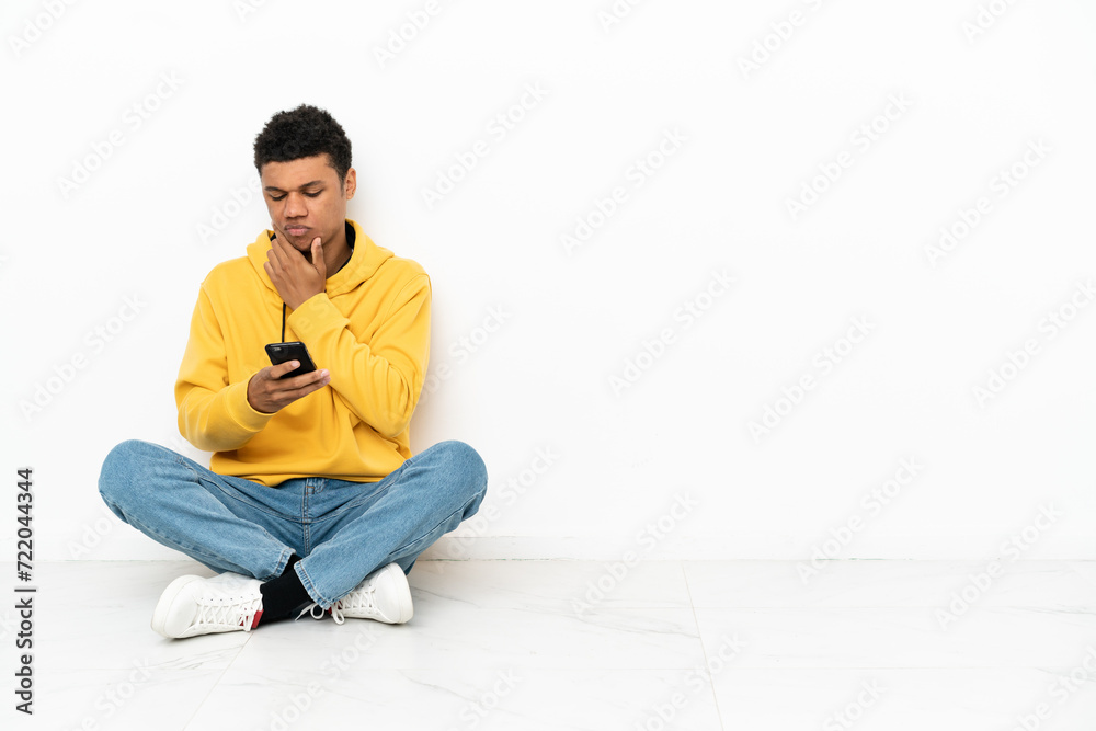 Young African American man sitting on the floor isolated on white background thinking and sending a message