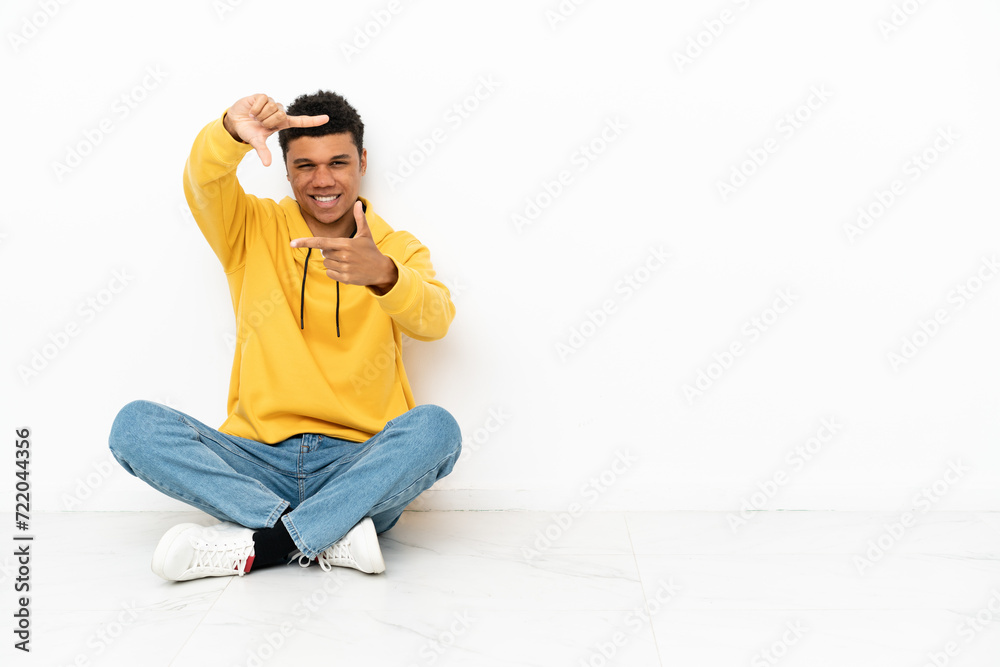 Young African American man sitting on the floor isolated on white background focusing face. Framing symbol Young African American man sitting on the floor isolated on white background focusing face. Framing symbol