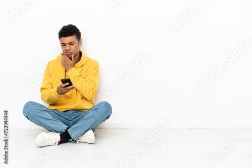 Young African American man sitting on the floor isolated on white background thinking and sending a message © luismolinero