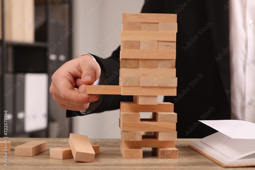 Playing Jenga. Man removing wooden block from tower at table indoors, closeup Playing Jenga. Man removing wooden block from tower at table indoors, closeup