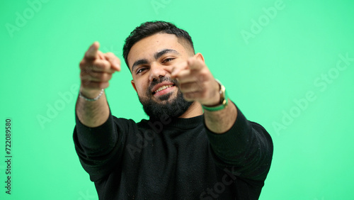 A man, close-up, on a green background, points forward