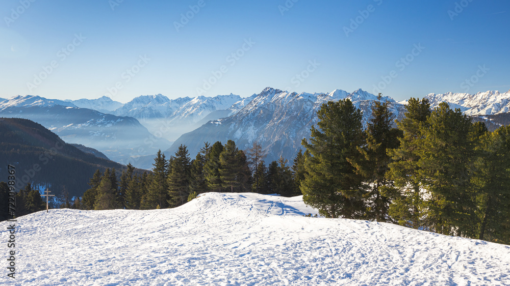 Snow-covered mountains with pine trees and blue sky in the backdrop, Tyrol, Austria