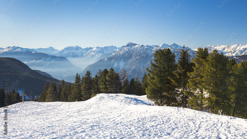 Fototapeta premium Snow-covered mountains with pine trees and blue sky in the backdrop, Tyrol, Austria