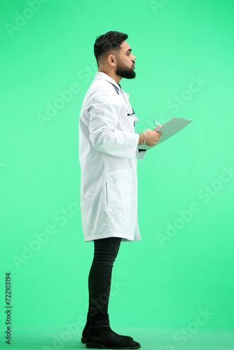 The doctor, in full height, on a green background, writes