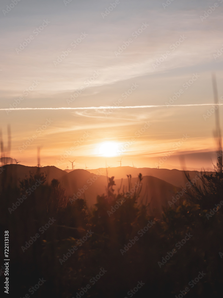Fototapeta premium Golden hour with the sun setting behind the rolling hills and wind turbines