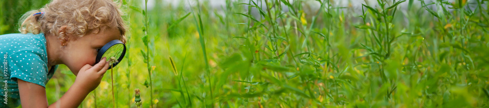 A child looks through a magnifying glass in nature. Selective focus. A child looks through a magnifying glass in nature. Selective focus.