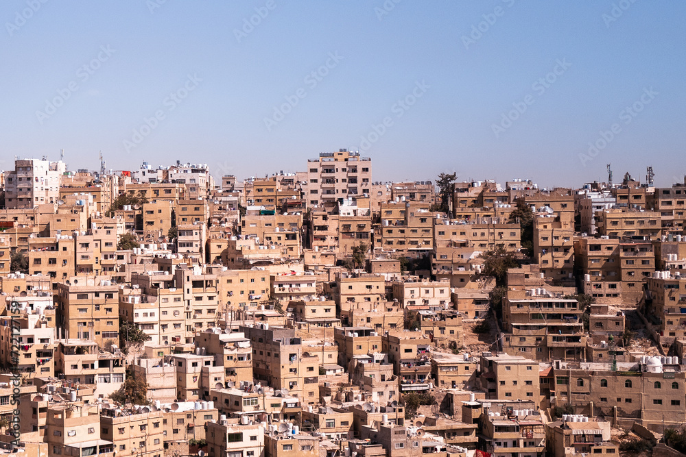 3x2 multiple high rise buildings in a Middle Eastern overpopulated neighbourhood. Flats are packed together like a puzzle with narrow alleyways. Warm sunny day blue sky. Amman, Jordan