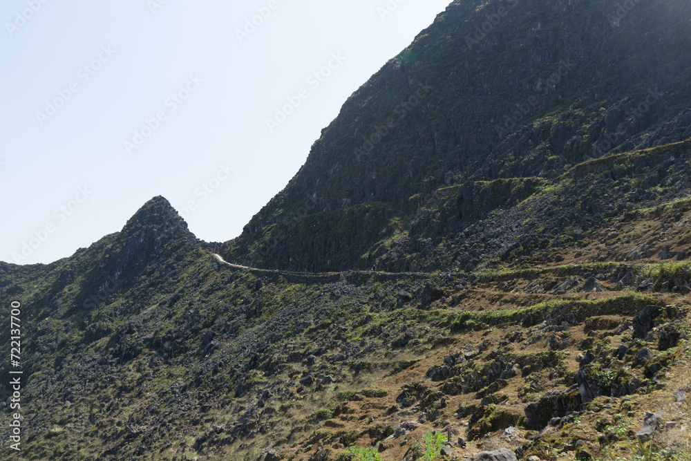 A winding mountain road traversing a rugged terrain under a bright sky