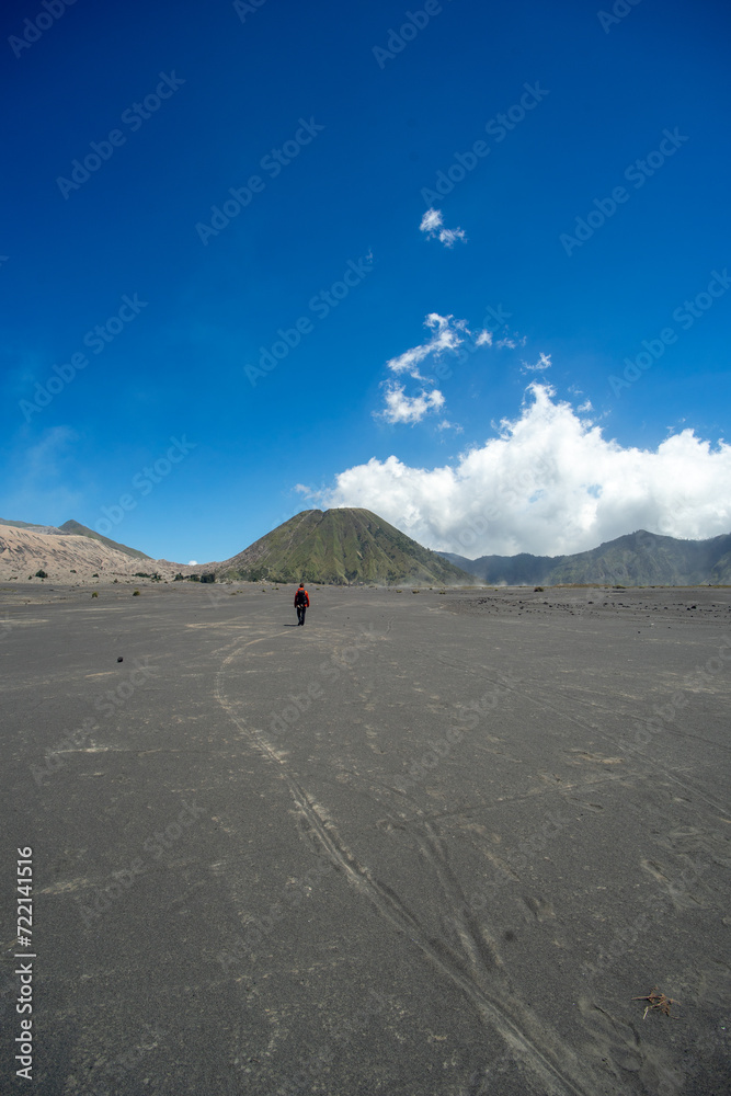 A lone traveler walking across a barren volcanic landscape under a clear blue sky