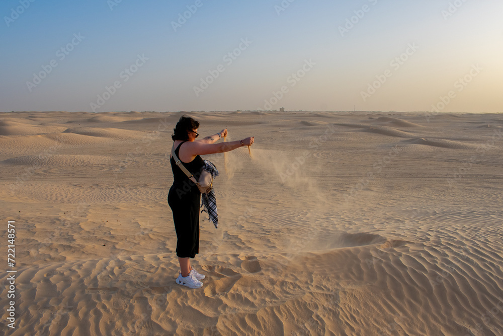 Side view of young woman, female tourist releasing sand from hands in sahara desert, Tunisia.  