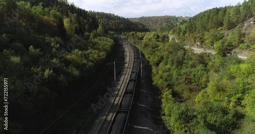 Freight long train carries with coal carriages on stone bridge by dangerous part of Trans Siberian railways near river in forest mountains. Aerial drone wide view at summer sunny sunset photo