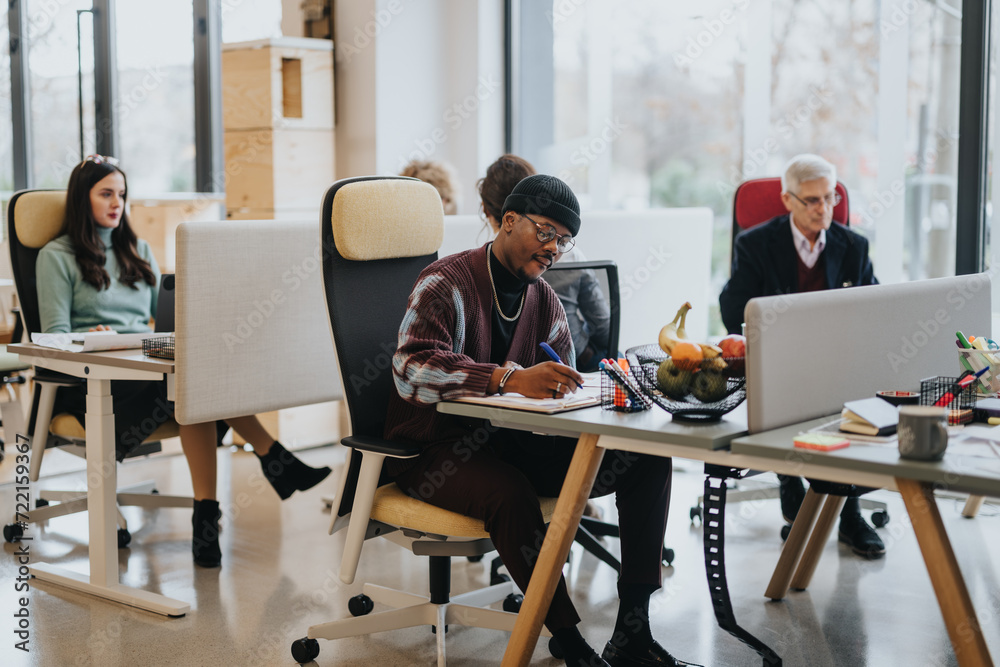 A multicultural office scene with focused employees working at desks. Men and women of various ages demonstrate teamwork and professionalism in a contemporary workspace. - obrazy, fototapety, plakaty 