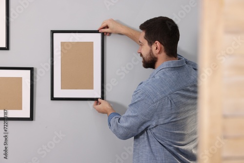 Man hanging picture frame on gray wall indoors