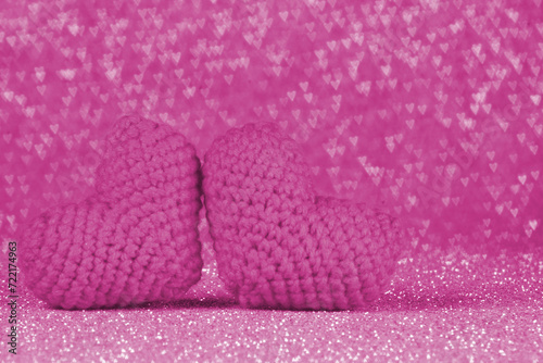 Two knitted pink heart on shiny pink backdrop. Heart shaped bokeh on background. Special day concept idea. Selective focus. Abstract background. 