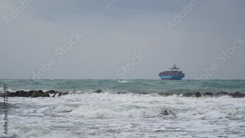 Cargo Ship with containers in stormy sea. Cloudy seascape, sea waves and Container vessel at horizon on the Mediterranean coast.