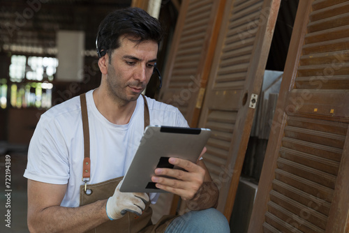 Portrait of male carpenter using digital tablet checking furniture at woodwork workshop. Male joiner working in furniture workshop. Start up and small business concept