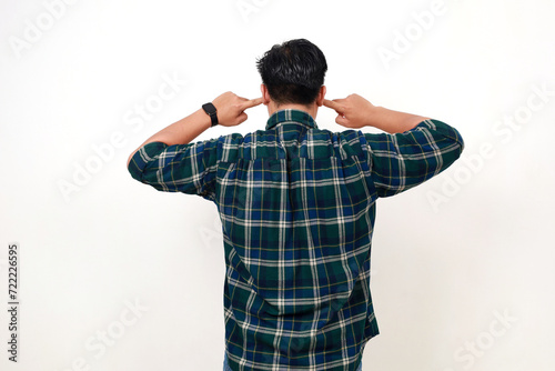 Back view of young asian man standing while covering his ears. Isolated on white