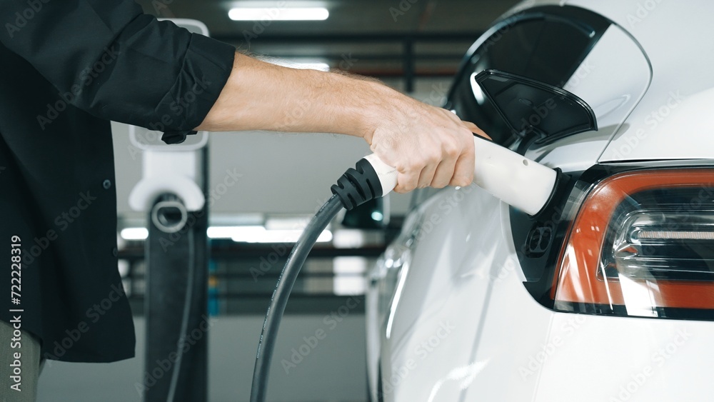 Young man travel with EV electric car to shopping center parking lot charging station in downtown city urban sustainability lifestyle by green clean rechargeable energy of electric vehicle innards