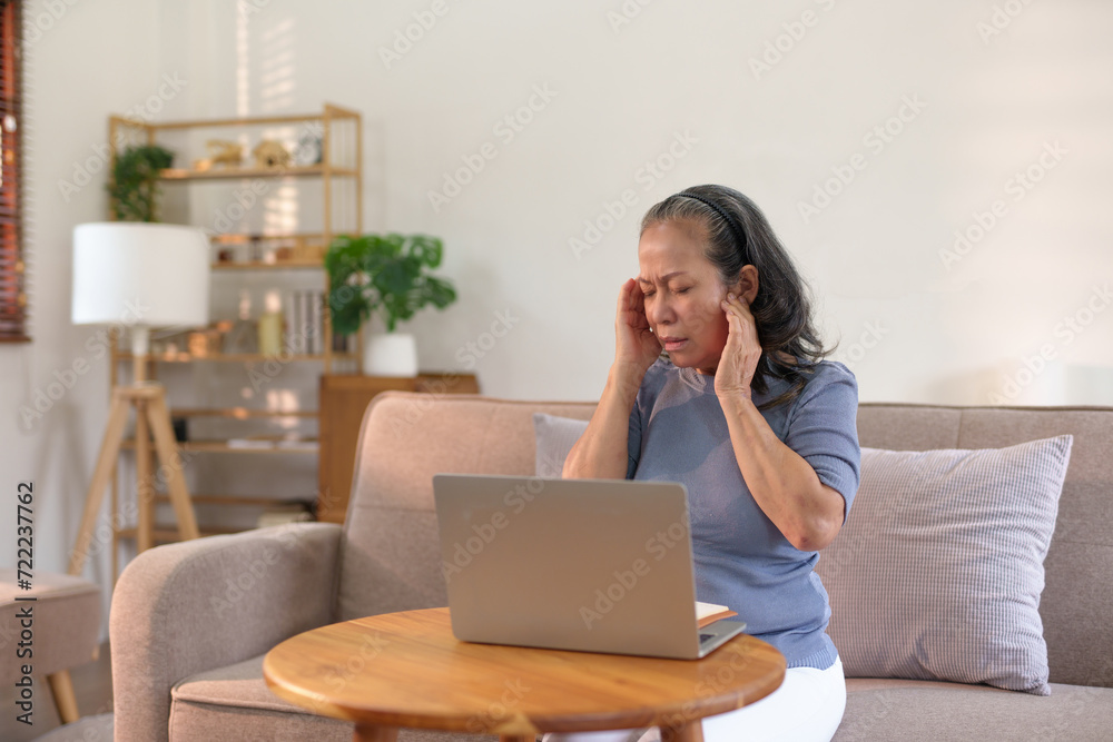 Older asian woman appears stressed and fatigued while working on a laptop from her home. Older asian woman appears stressed and fatigued while working on a laptop from her home.
