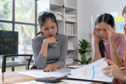Three young asian businesswomen appear concerned while closely examining financial reports, indicating a challenging business analysis session.