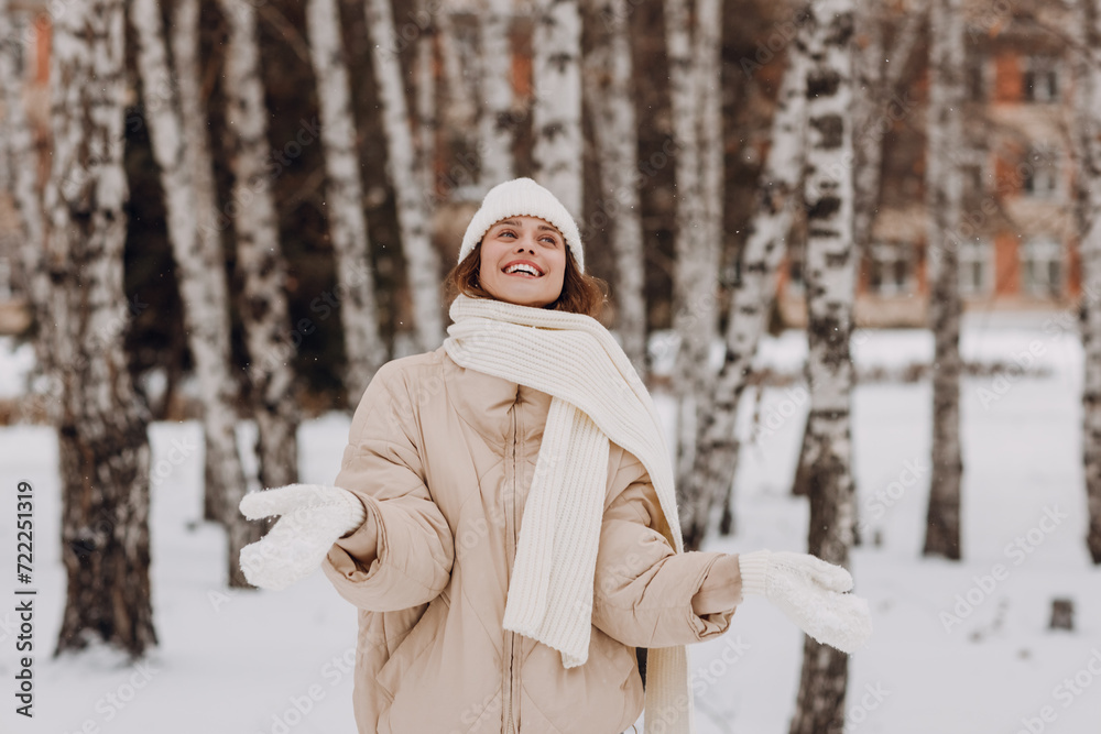 Obraz premium Young smiling woman dressed coat scarf hat and mittens enjoys winter weather at birch winter park