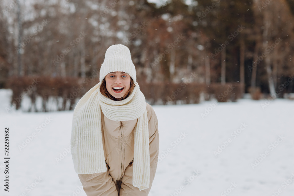 Obraz premium Happy smiling young woman portrait dressed coat scarf hat and mittens enjoys winter weather at snowy winter park