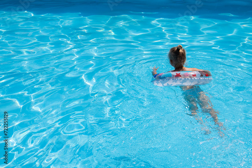 Child girl learn to swim with an inflatable ring in the pool
