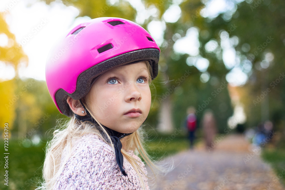 Sad child girl in a pink helmet in the park Sad child girl in a pink helmet in the park