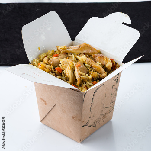 Pilaf with chicken meat, carrots, tomatoes, onions and herbs in paper box.