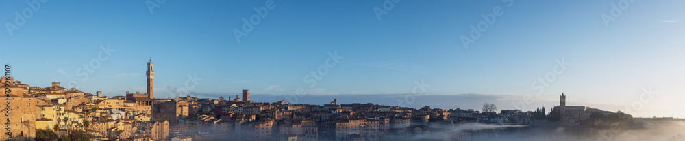 Foggy sunrise in Siena, Italy, panorama with Torre del Mangia and the Church of Santa Maria dei Servi