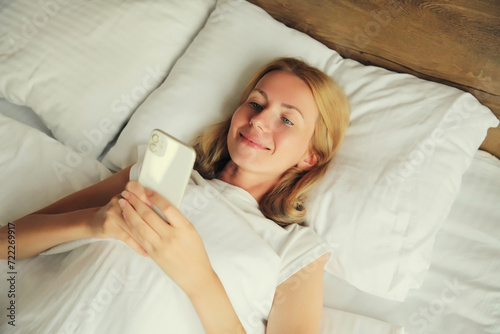 Happy relaxed young woman with mobile phone lying in bed at home