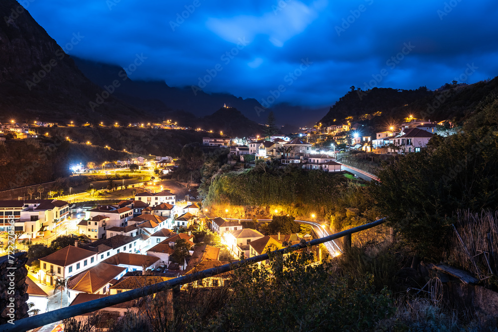 The night-time atmosphere, street lighting and car light trails of the picturesque village on the north coast in a green, overgrown valley. Sao Vincente, Madeira Island, Portugal, Europe.