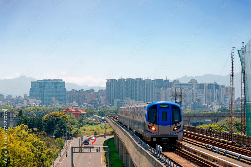 Naklejka premium Scenic view of a metro train traveling on elevated rails of Taoyuan Airport MRT System and residential buildings clustering in background under blue clear sky in Zhongli, Taoyuan City, Taiwan, Asia