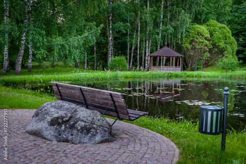 Bench to relax in a shady green park with fountain in the pond. Smiltene Old Park, Latvia. photo