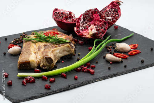 Grilling steak with pepper, rosemary, onion, garlic and pomegranate on a black board and on the white background