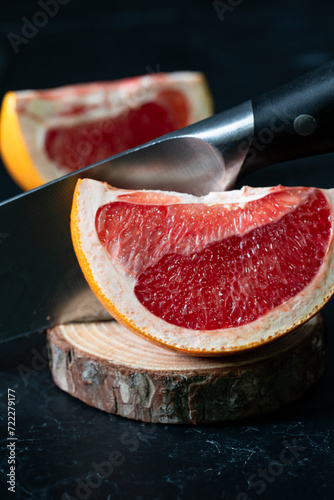 Two pieces of grapefruit cutting with a knife on a wooden board