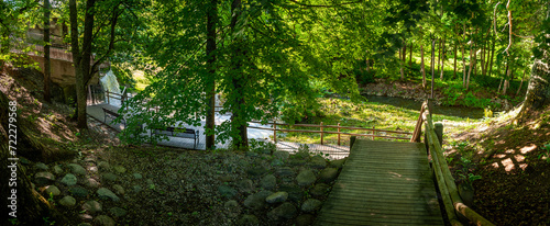 Along the trail is a sitting bench looking out at waterfall and park in a shaded area in summertime. Peaceful place to solitude and relax. Vecais parks  Smiltene  Latvia.