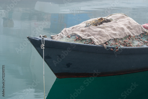 Grado, Italy - January 28th, 2024: a small fishing boat with fishing nets on the bow in the Mandracchio port on a winter day with thick fog. photo