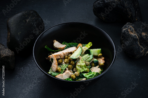 Meat salad with chicken slices, cucumber, lettuce and green peas in bowl.