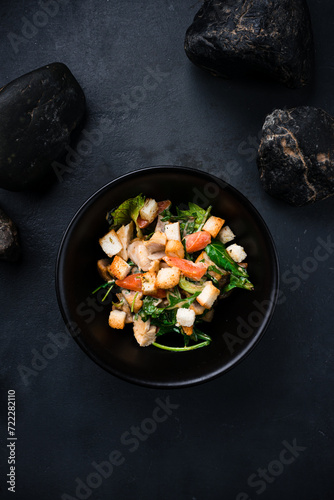 Fresh salad with chicken, carrot, arugula, lettuce and croutons on a dark table.