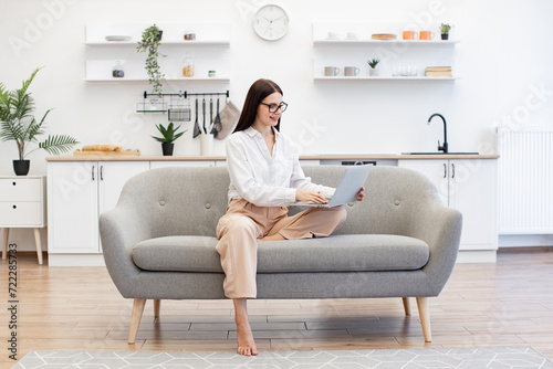 Free Download Focused caucasian woman dressed in casual attire typing on wireless laptop while sitting on comfy sofa. Attractive brunette female freelancer doing online work while staying at home. - GFXLoad
