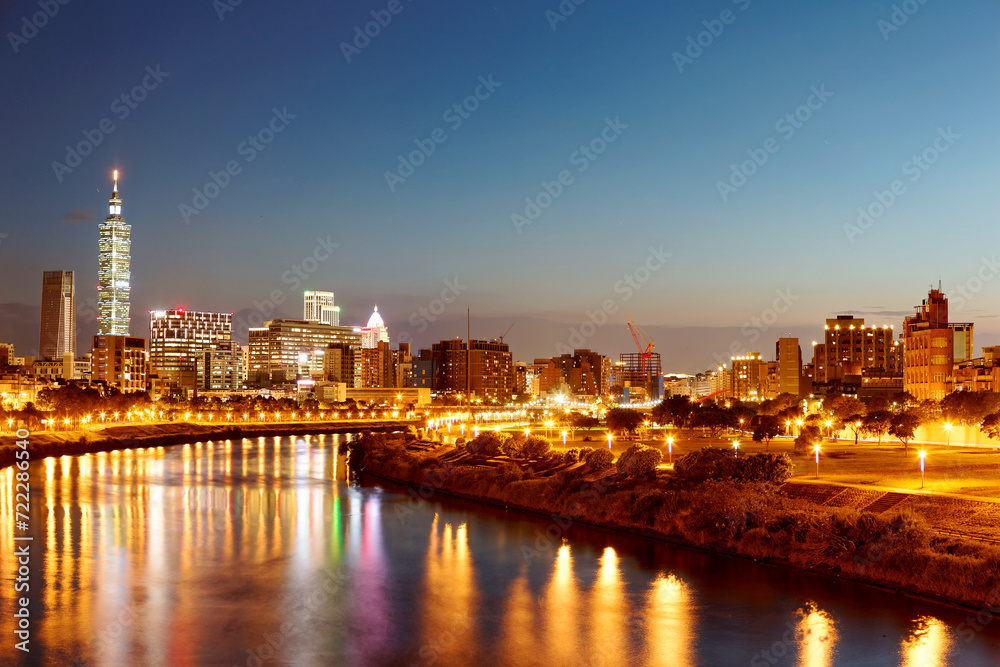 Obraz premium Riverside urban skyline of Taipei, the vibrant capital city of Taiwan, with landmark 101 Tower among modern skyscrapers in Xinyi District and city lights reflected on Keelung River in evening twilight