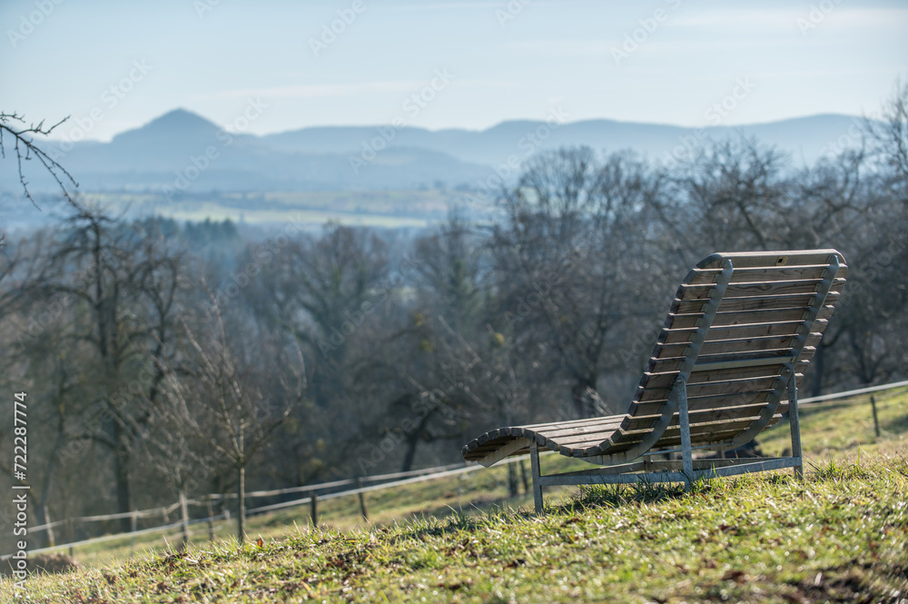 Fototapeta premium Holzliege an Aussichtspunkt an der Rieter Steige zwischen Altenriet und Neckartenzlingen mit Blick auf Hügelkette der schwäbischen Alb mit Reutlinger Hausberg Achalm.
