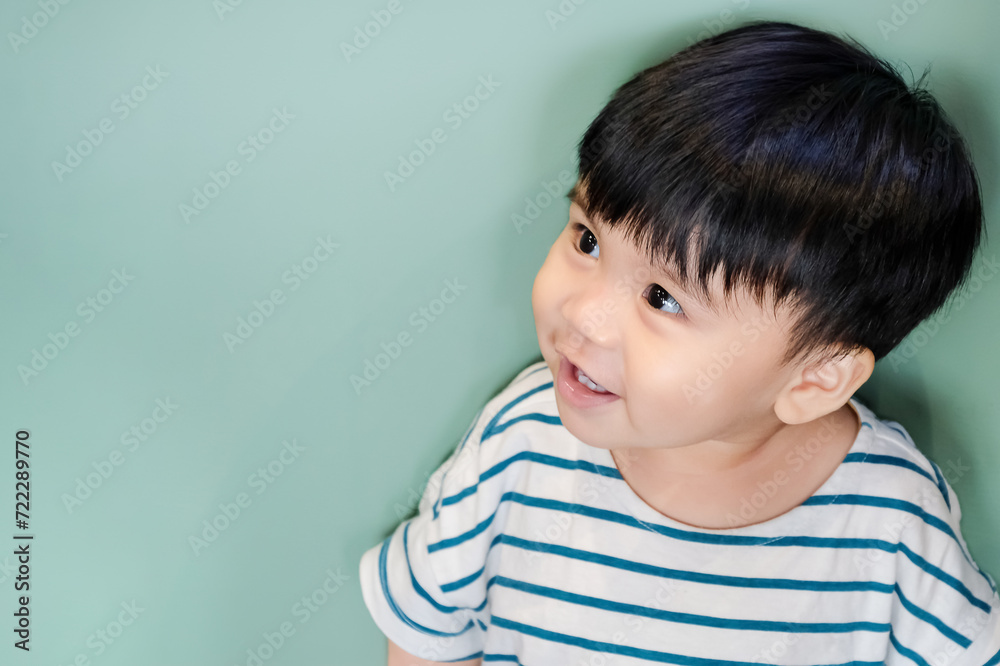 Smiling asian baby toddler looking up isolated on pastel green background with copy space Smiling asian baby toddler looking up isolated on pastel green background with copy space